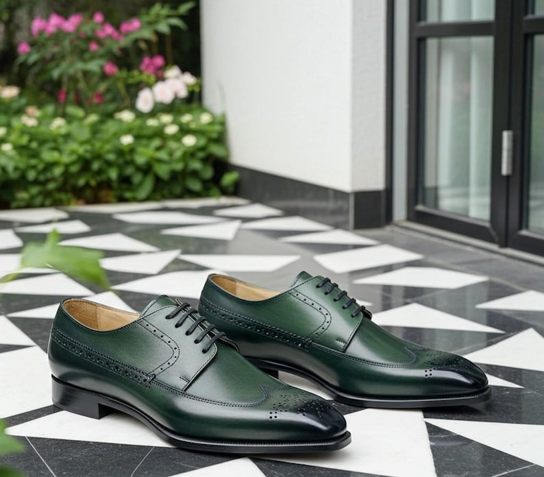 May include: A pair of green leather dress shoes with black laces and black toe caps. The shoes have decorative perforations and are displayed on a black and white tiled surface. The shoes are a classic style.