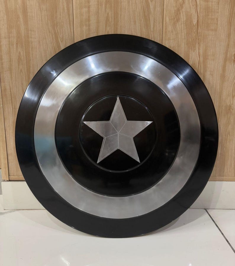 May include: A black and silver shield featuring a central silver star. The shield has a circular design with black and silver concentric rings. The star is positioned on a black background.