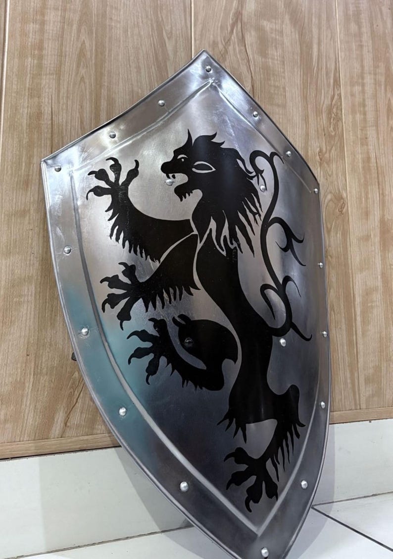 Pu&ograve; includere: Uno scudo color argento con un emblema di leone nero. Lo scudo ha una parte superiore arrotondata ed &egrave; bordato da rivetti. Il leone &egrave; raffigurato in stile araldico, con una zampa alzata e una criniera fluente. Lo scudo &egrave; appoggiato contro una superficie di legno.