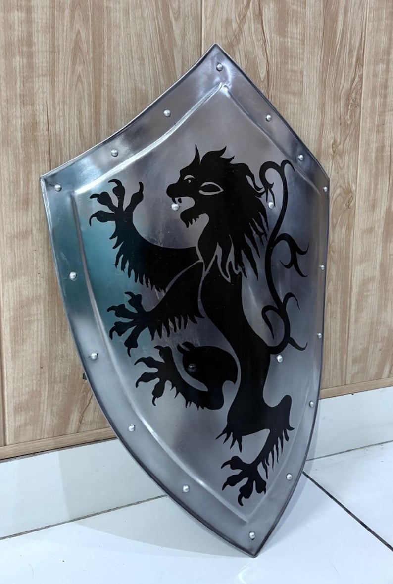 Pu&ograve; includere: Scudo color argento con un emblema di leone nero. Lo scudo &egrave; rivettato sui bordi e ha una base appuntita. Il leone &egrave; raffigurato in stile araldico, con un'espressione feroce e le zampe sollevate. Lo scudo &egrave; probabilmente in metallo.