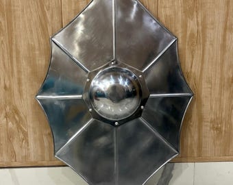 Può includere: Uno scudo in stile medievale di colore argento con un design unico e sfaccettato. Lo scudo presenta un boss centrale arrotondato ed è costruito con più pannelli metallici. Lo scudo è esposto su uno sfondo di legno.