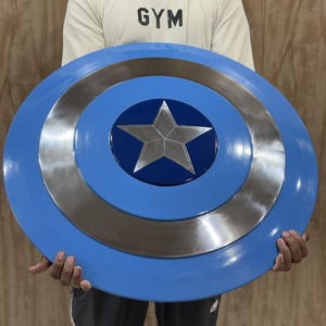 May include: A circular shield featuring a concentric design with a bright blue outer ring, a metallic silver middle ring, and a dark blue center circle. A prominent five-pointed silver star is centered within the dark blue circle.