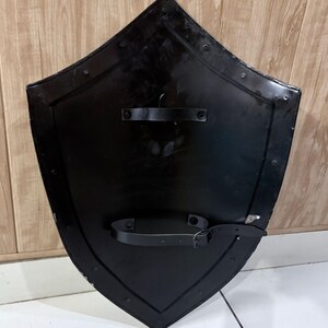 Pu&ograve; includere: Uno scudo nero con la parte superiore a punta e i lati curvi. Il retro dello scudo presenta due cinghie in pelle e una fibbia per fissarlo. Lo scudo &egrave; in metallo e ha una finitura lucida.