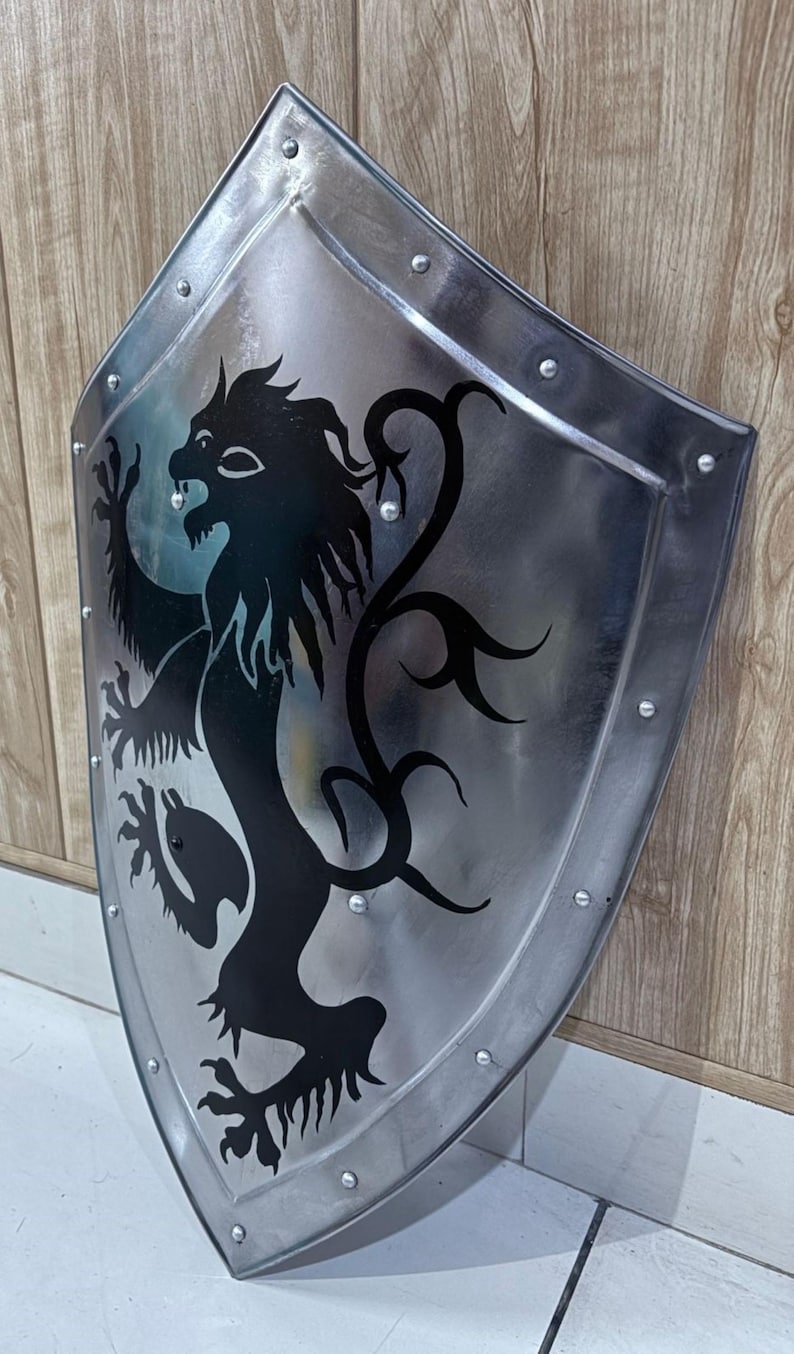 Pu&ograve; includere: Uno scudo color argento con un emblema di leone nero. Lo scudo ha una parte superiore arrotondata e una inferiore a punta, con rivetti sul bordo. Il leone &egrave; raffigurato in stile araldico.