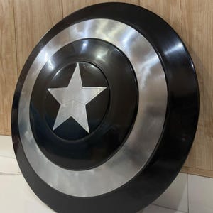 May include: A circular shield in black and silver, featuring a central silver star. The design includes a silver band and a black outer edge. This shield is likely a prop or collector's item.