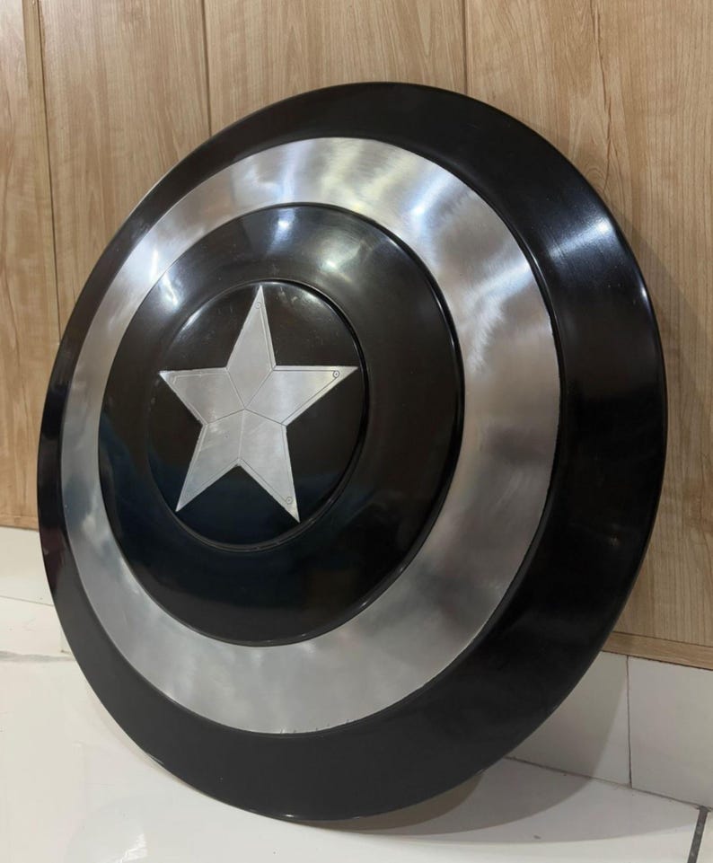 May include: A circular shield in black and silver, featuring a central silver star. The design includes a silver band and a black outer edge. This shield is likely a prop or collector's item.