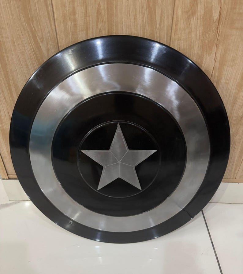 May include: A circular shield featuring a black and silver design. The shield has a central silver star and concentric circles in black and silver. This shield is a prop or collectible item.