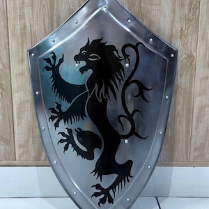 Może przedstawiać: Srebrna tarcza z czarnym herbem lwa. Tarcza ma spiczaste dno i jest obramowana nitami. Lew jest w pozie heraldycznej, z uniesionymi przednimi łapami. Tarcza jest prawdopodobnie wykonana z metalu.