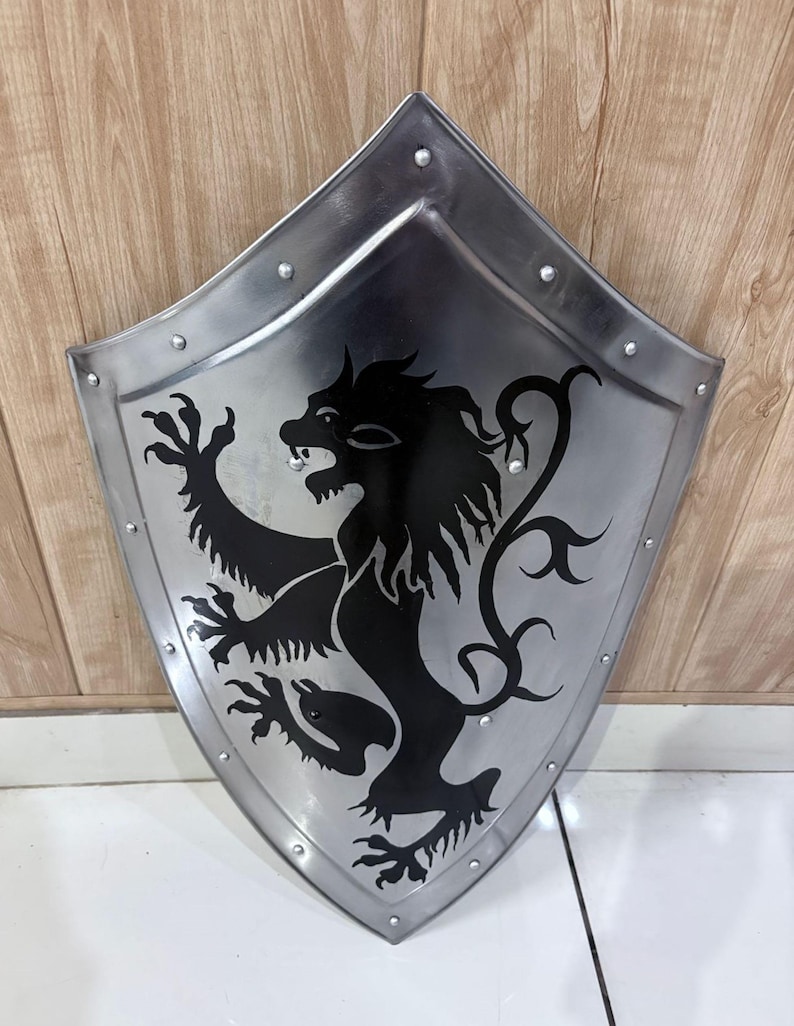 Pu&ograve; includere: Uno scudo color argento con un emblema di leone nero. Lo scudo ha una parte superiore arrotondata e una inferiore a punta, con rivetti lungo i bordi. Il leone &egrave; raffigurato in stile araldico.