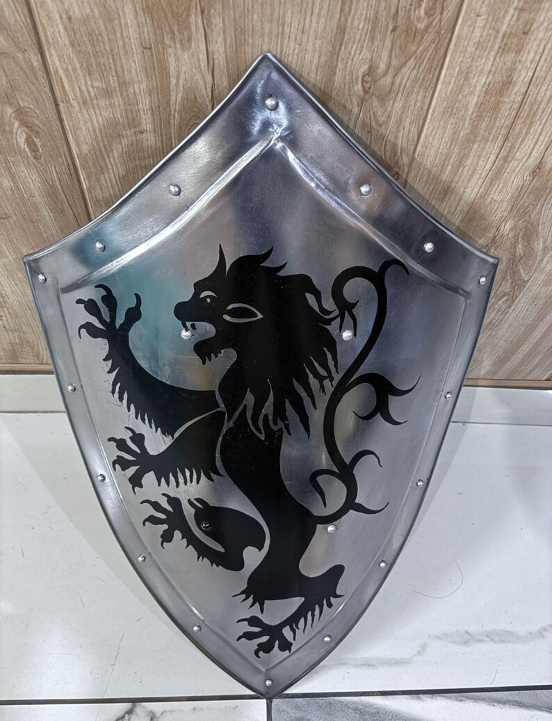 Pu&ograve; includere: Uno scudo in metallo color argento con un emblema di leone nero. Lo scudo ha una parte superiore a punta e una base arrotondata, con rivetti lungo i bordi. Il leone &egrave; raffigurato in stile araldico, con una zampa alzata e una criniera fluente.