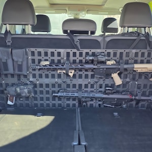 May include: Black tactical vehicle seat organizer with multiple pouches and a grid system for mounting firearms and accessories. Includes two rifles, a handgun, and various attachments. The organizer is designed to fit behind the rear seats.