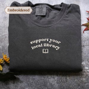 A gray t-shirt with the text "Support your local library" printed on it, along with a small book icon.