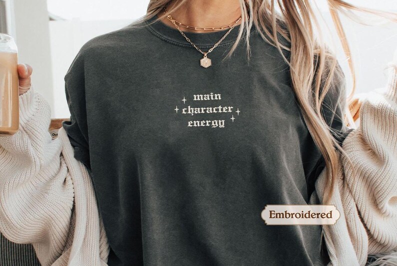 A person wearing a gray sweatshirt with the text "main character energy" printed on it.