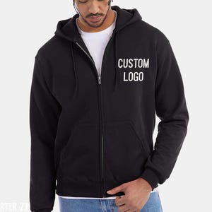 A man wearing a black hooded sweatshirt with the text "CUSTOM LOGO" printed on it.