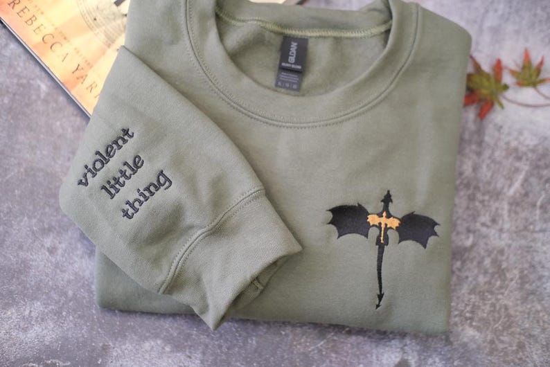 A grey sweatshirt with a dragon embroidered on the front, along with the text "Violent little thing" printed on the left sleeve.