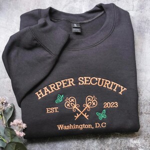 A black sweatshirt with text and graphics printed on it, laid out on a gray surface.