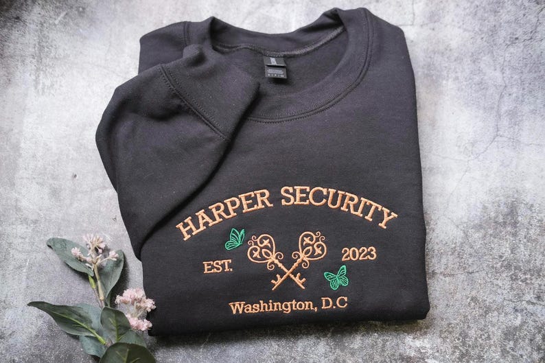 A black sweatshirt with text and graphics printed on it, laid out on a gray surface.
