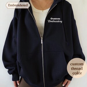 A close-up of a navy blue hooded sweatshirt with the text "Embroidered" and "Custom Embroidery" printed on it.