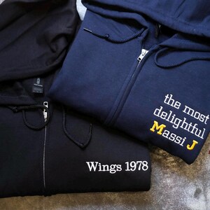 two hooded sweatshirts, one black and one navy blue, with the navy blue one having text on it.