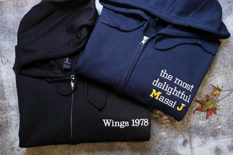 two hooded sweatshirts, one black and one navy blue, with the navy blue one having text on it.