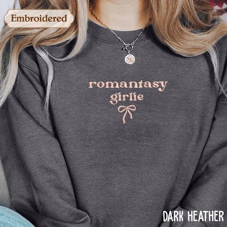 A close-up of a person wearing a gray sweatshirt with the text "romantic girl lie" embroidered on it.