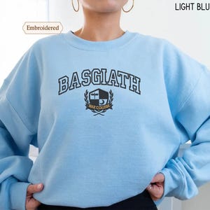 A person wearing a light blue sweater with the text "BASGIATH WAR COLLEGE" printed on it.