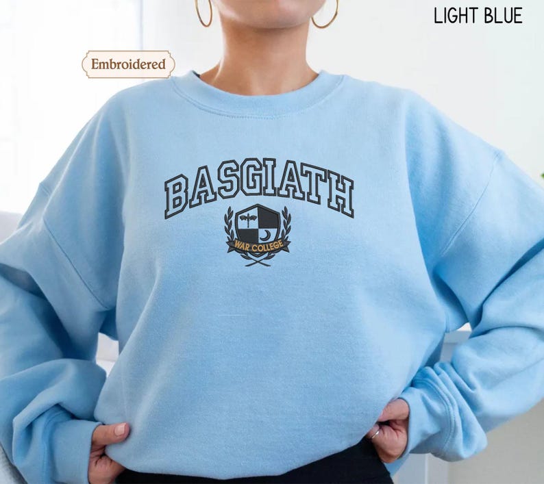 A person wearing a light blue sweater with the text "BASGIATH WAR COLLEGE" printed on it.
