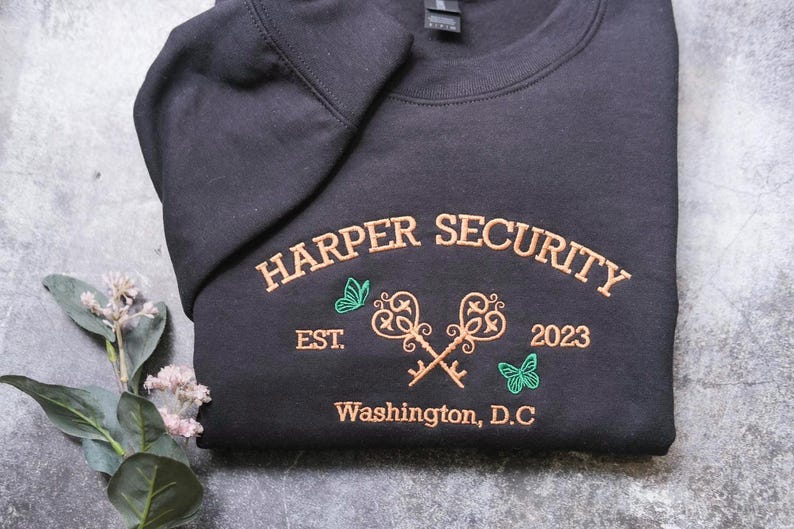 A black t-shirt with gold text and graphics, including the words "Harper Security" and "Est. 2023 Washington, D.C."