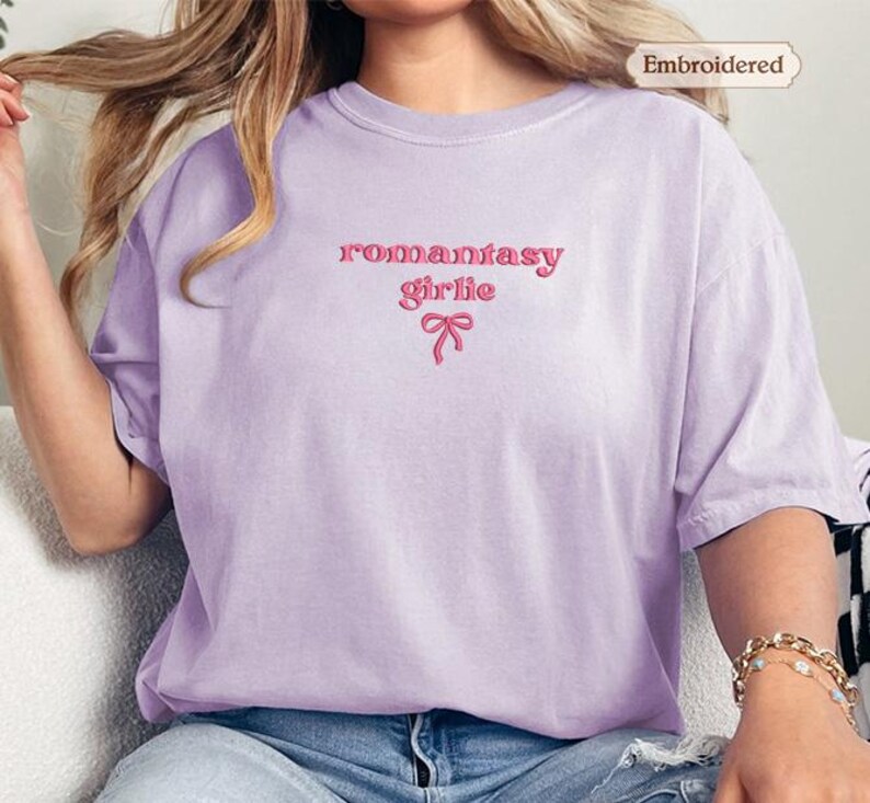 A woman wearing a purple t-shirt with the text "romantic girl" embroidered on it.