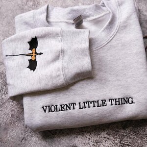 A gray sweatshirt with a dragon design and the text "VIOLENT LITTLE THING" printed on it.