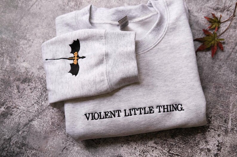 A gray sweatshirt with a dragon design and the text "VIOLENT LITTLE THING" printed on it.