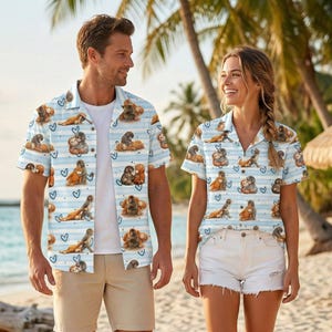 Può includere: Camicie azzurre con bottoni con un motivo di scimmie marroni, cuori e strisce blu. Le camicie hanno maniche corte e sono indossate da due persone su una spiaggia. Set coordinato.