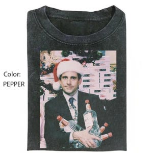 May include: Pepper-coloured t-shirt with a graphic of a man in a Santa hat holding bottles. The image has a vintage, slightly faded appearance. The man is wearing a suit and tie, with a Christmas tree in the background.