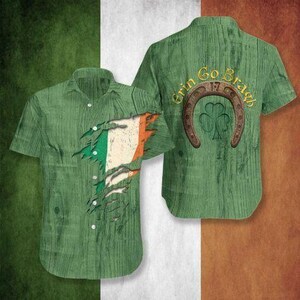 May include: Green short-sleeved shirt with a wood grain texture. The front features a torn design revealing the Irish flag. The back displays a horseshoe, a shamrock, and the words "Erin Go Bragh" in gold lettering. The shirt is a St. Patrick's Day theme.