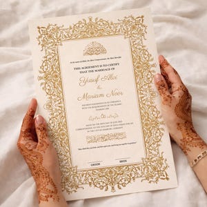 May include: A cream-colored marriage certificate with ornate gold filigree border and text. The document certifies the marriage of Yusuf Alvi and Mariam Noor. The hands holding the certificate have henna designs.