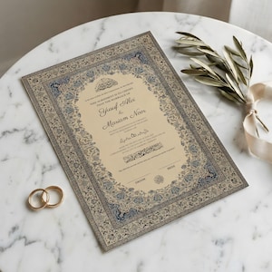 Pode incluir: Um certificado de casamento com uma borda floral azul e bege ornamentada, com os nomes de Yusuf Alvi e Mariam Noor. Duas alianças de casamento douradas estão no canto inferior esquerdo. Um raminho de vegetação e uma fita estão à direita.