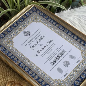 Peut inclure: Certificat de mariage encadré avec une bordure dorée. Le document présente des motifs bleus et dorés ornés, avec les noms Yusuf Alvi et Mariam Noor. Deux alliances dorées sont visibles.