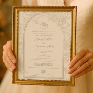 May include: A framed marriage certificate with gold trim is held up. The certificate has a cream background with floral accents and text in English and Arabic. The names "Yusuf Alex" and "Mariam Noor" are visible.