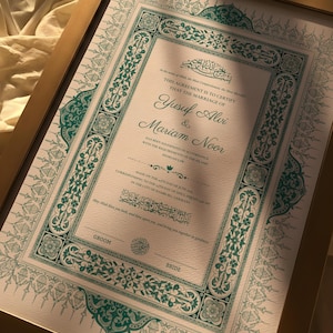 May include: A framed marriage certificate with teal and gold decorative elements. The document includes Arabic script and the names Yusuf Alvi and Mariam Noor. The frame is gold, and the background is a soft, neutral colour.
