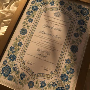May include: Framed marriage certificate with gold trim, featuring floral designs in blue and green. The document includes text in English and Arabic, with the names Yusuf Alvi and Mariam Noor. A decorative piece for a wedding.