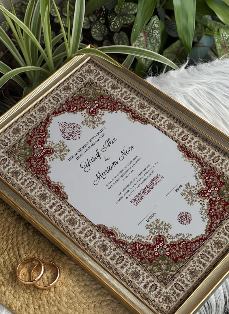 May include: A framed marriage certificate with a gold border. The document includes the names Yusuf Alvi and Mariam Noor, with decorative red, green, and brown borders. Two gold wedding rings are in the foreground.