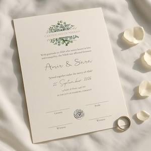 以下が含まれることがあります： 「CERTIFICATE OF NIKKAH」の文字と「Amir & Sara」の名前が記載されたクリーム色の証明書。日付「2026年9月25日」も表示されています。金の指輪と白い花びらが証明書の周りに散らばっています。