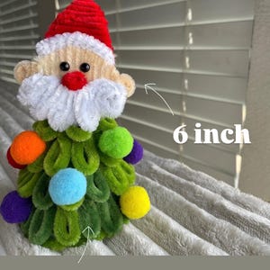 May include: A handmade Christmas tree ornament shaped like Santa Claus. The Santa has a red hat, white beard, and a green tree-shaped body. The tree is decorated with colorful pom-poms. The ornament is approximately 6 inches tall and 4 inches wide.