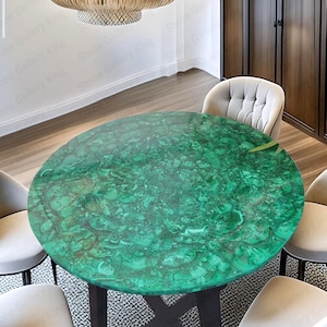 May include: A circular dining table featuring a striking green malachite surface. The table is supported by a dark base and surrounded by four cream-coloured chairs. The table's surface has a distinctive, swirling pattern. A modern chandelier hangs above.
