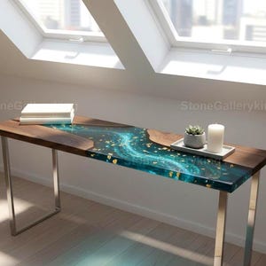 Könnte beinhalten: Ein moderner, rechteckiger Holzschreibtisch mit einem türkisfarbenen Harzfluss-Design und Goldblatt-Akzenten. Der Schreibtisch hat einen dunklen Holzrahmen und silberne Metallbeine. Eine kleine Sukkulente, eine weiße Kerze und Bücher liegen oben.