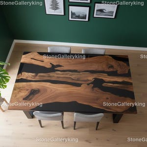 Könnte beinhalten: Ein großer, rechteckiger Esstisch aus Holz mit einer dunklen Epoxidharz-Einlage. Der Tisch hat ein natürliches Holzmaserungsmuster mit dunkelbraunen und schwarzen Tönen. Der Tisch wird von dunklen Beinen getragen und ist von grauen Stühlen umgeben.