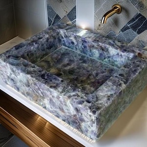 Könnte beinhalten: Ein rechteckiges Waschbecken aus Amethyststein mit poliertem Innenraum. Das Waschbecken steht auf einer weißen Arbeitsplatte mit einem Holzschrank darunter. Ein goldener Wasserhahn ist an der Wand über dem Waschbecken montiert. Maße: 61 cm breit und 46 cm tief.