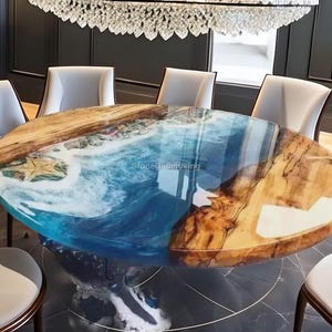 May include: Oval dining table with a unique design. The tabletop features a blue and white ocean-themed resin design, combined with natural wood grain. The table is supported by a dark base and surrounded by white chairs. The table is approximately 72 inches long.