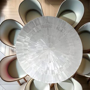 Könnte beinhalten: Draufsicht auf einen runden weißen Tisch, umgeben von sechs cremefarbenen Stühlen. Der Tisch hat ein radiales Muster, und die Stühle haben Holzbeine und ein geschwungenes Rückendesign. Die Stühle sind um den Tisch angeordnet.