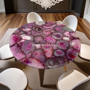 May include: A round table with a vibrant pink and purple agate stone top. The table has a light wood base with three legs. The table is surrounded by white chairs. The text "Stone Galleryking" is visible on the table.